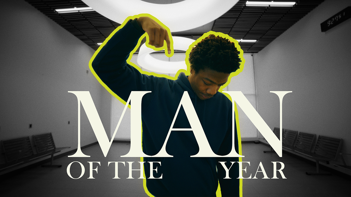 A person in a dimly lit room points downwards, highlighted by a bright outline. Bold text overlays: "Man of the Year," conveying confidence and achievement.